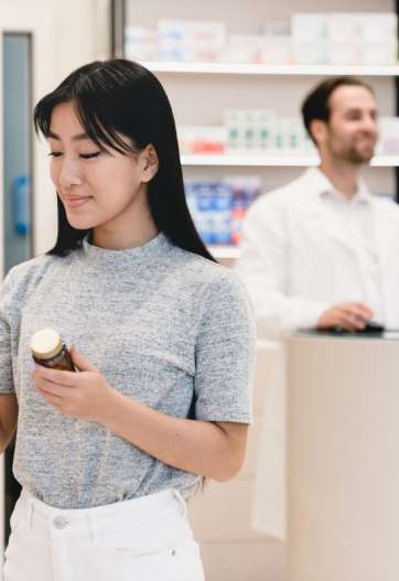 Female asian young client customer buyer checking information about side effects, ingredients, active substance in smart phone cellphone in drugstore pharmacy