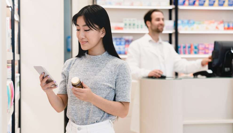 Female asian young client customer buyer checking information about side effects, ingredients, active substance in smart phone cellphone in drugstore pharmacy