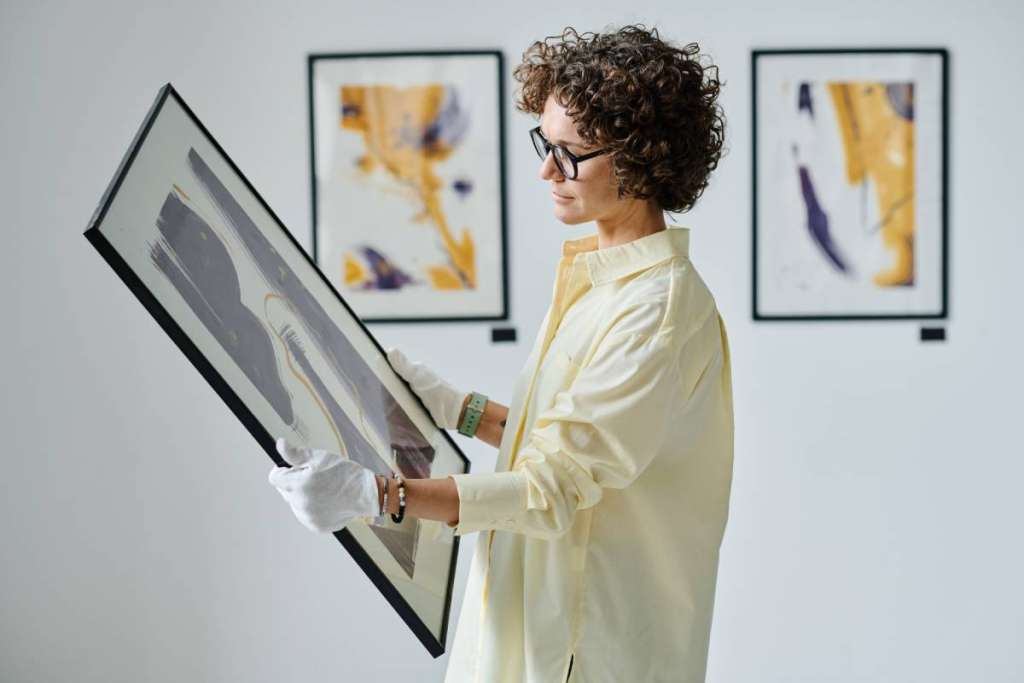 Young woman working with art at gallery, she standing and examining picture in frame in her hands